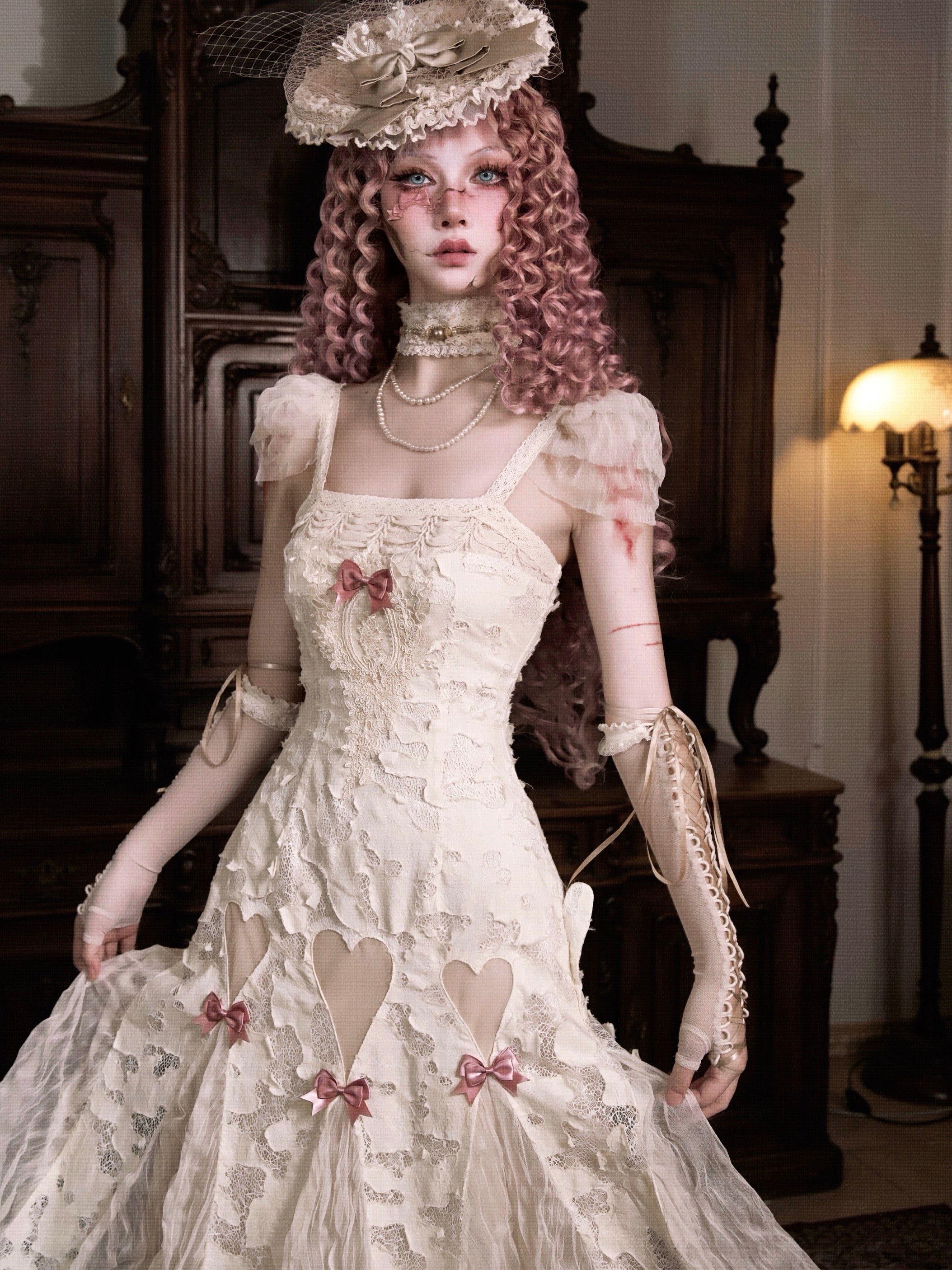 woman in a vintage-style lace white dress with pink ribbon details in a dimly lit room.