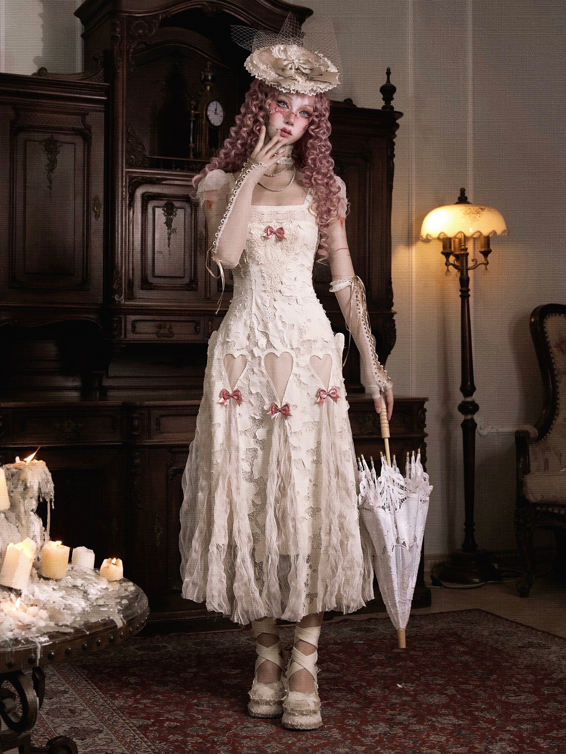 Woman in a vintage-style dress holding an umbrella in a room with ornate furniture and a lamp.