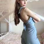 Young lady wearing a 1997 vintage styled blue denim romper with a tie at the waist and a keyhole back design, posing in a room with a pink aesthetic.