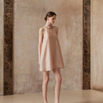 Woman wearing a beige dress standing against a textured wall.