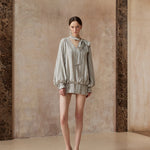 Woman wearing a light-colored outfit with a bow in a room with textured walls.