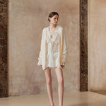 Woman wearing a white outfit standing against a textured wall.