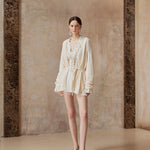 Woman wearing a light-colored dress standing against a textured wall.