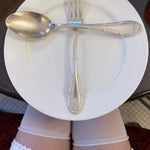 Person wearing white underwear with a white plate, spoon, and fork arranged in a manner resembling underwear.