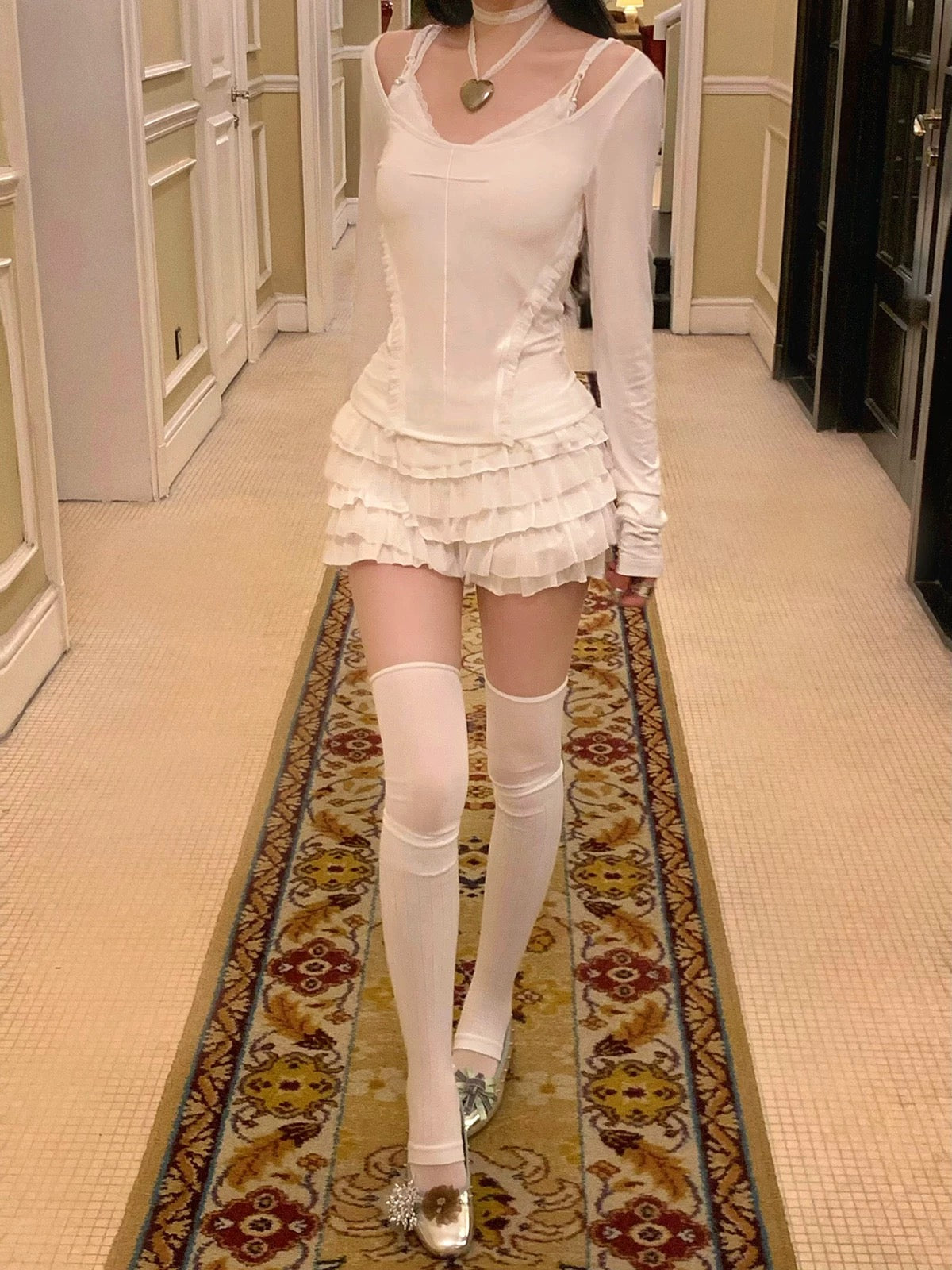 Person wearing a white dress with sheer sleeves and a ruffled skirt KittenClaw White Dream Cross Set, standing on a gothic patterned rug for halloween.