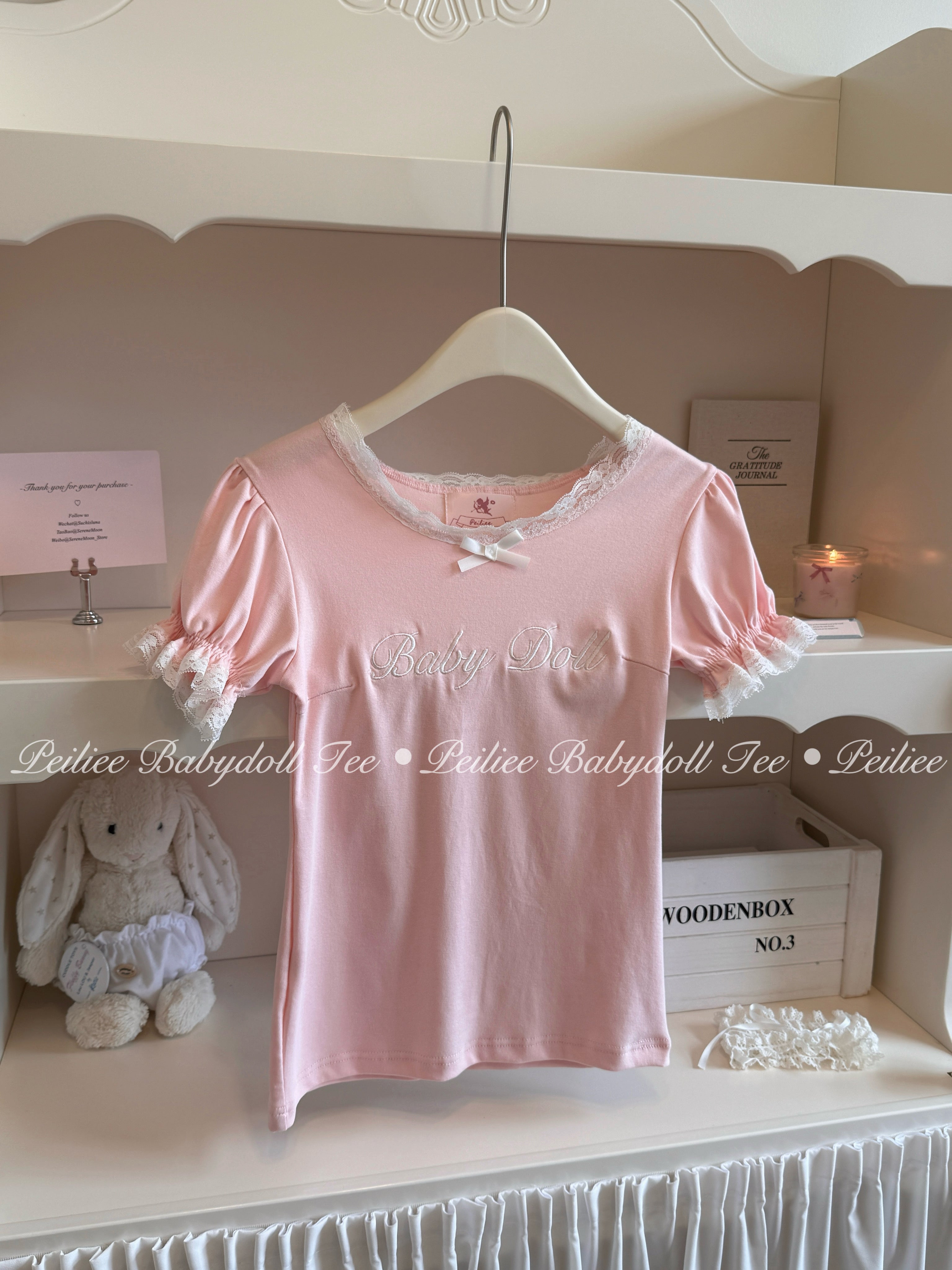 Pink babydoll top with lace details on a hanger against a white background