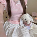 Girl wearing a pink peiliee design cottonn babydoll top and white skirt holding a plush bunny.