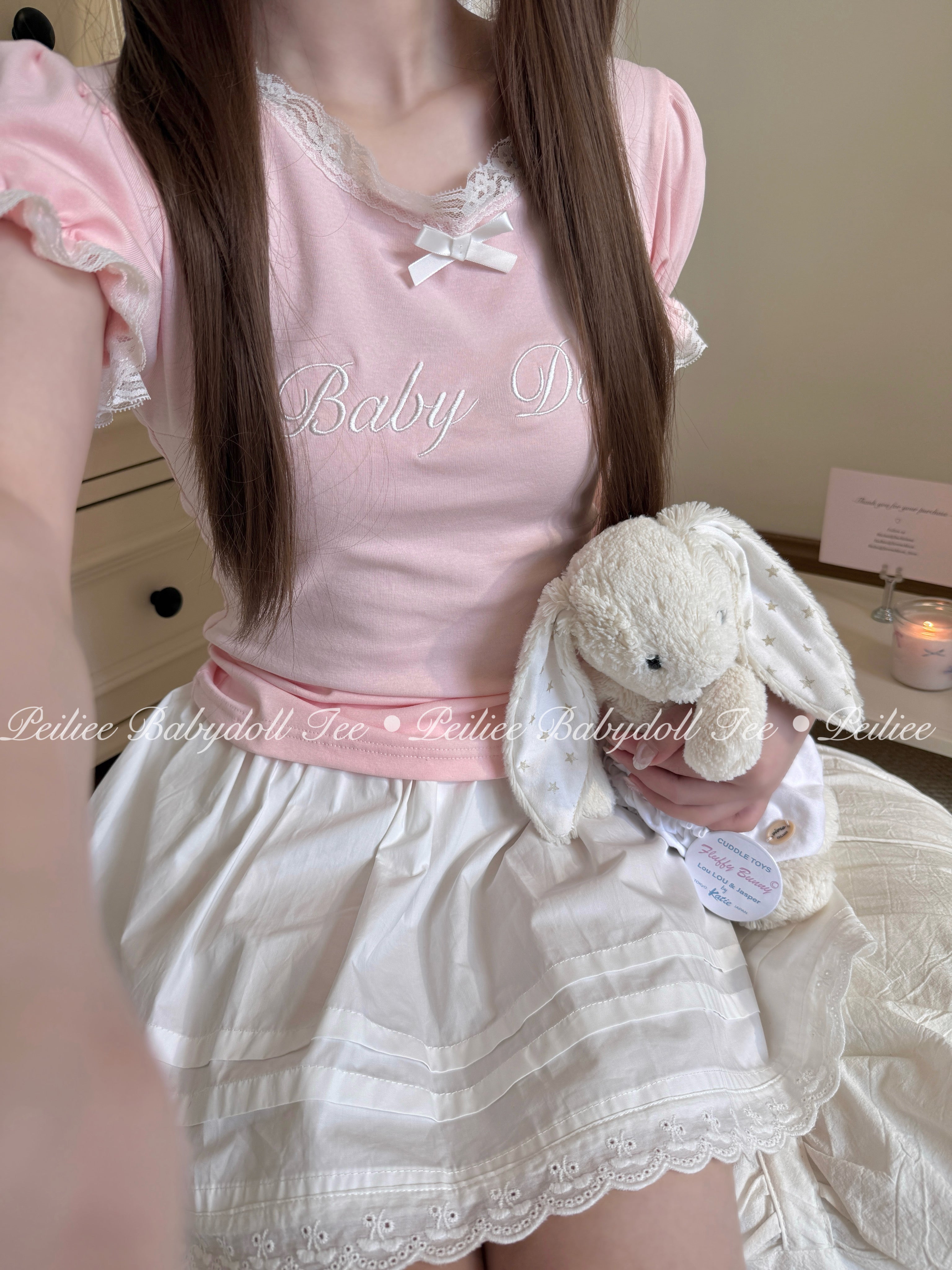 Girl wearing a pink peiliee design cottonn babydoll top and white skirt holding a plush bunny.