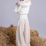 Woman wearing a white outfit with faux fur hoodie with sheep pattern standing on a pile of hay.