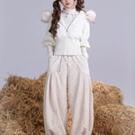 A Girl wearing a white outfit with faux fur hood and pants, standing on hay bales.