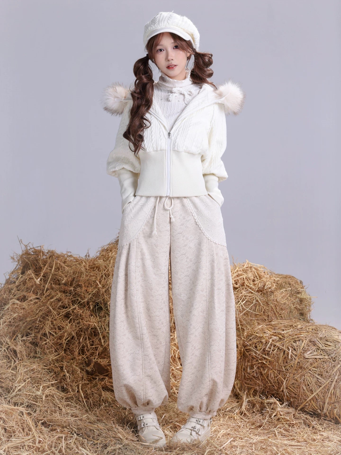 A Girl wearing a white outfit with faux fur hood and pants, standing on hay bales.