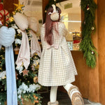 Girl wearing a checkered coat and white gloves in front of a decorated Christmas tree.