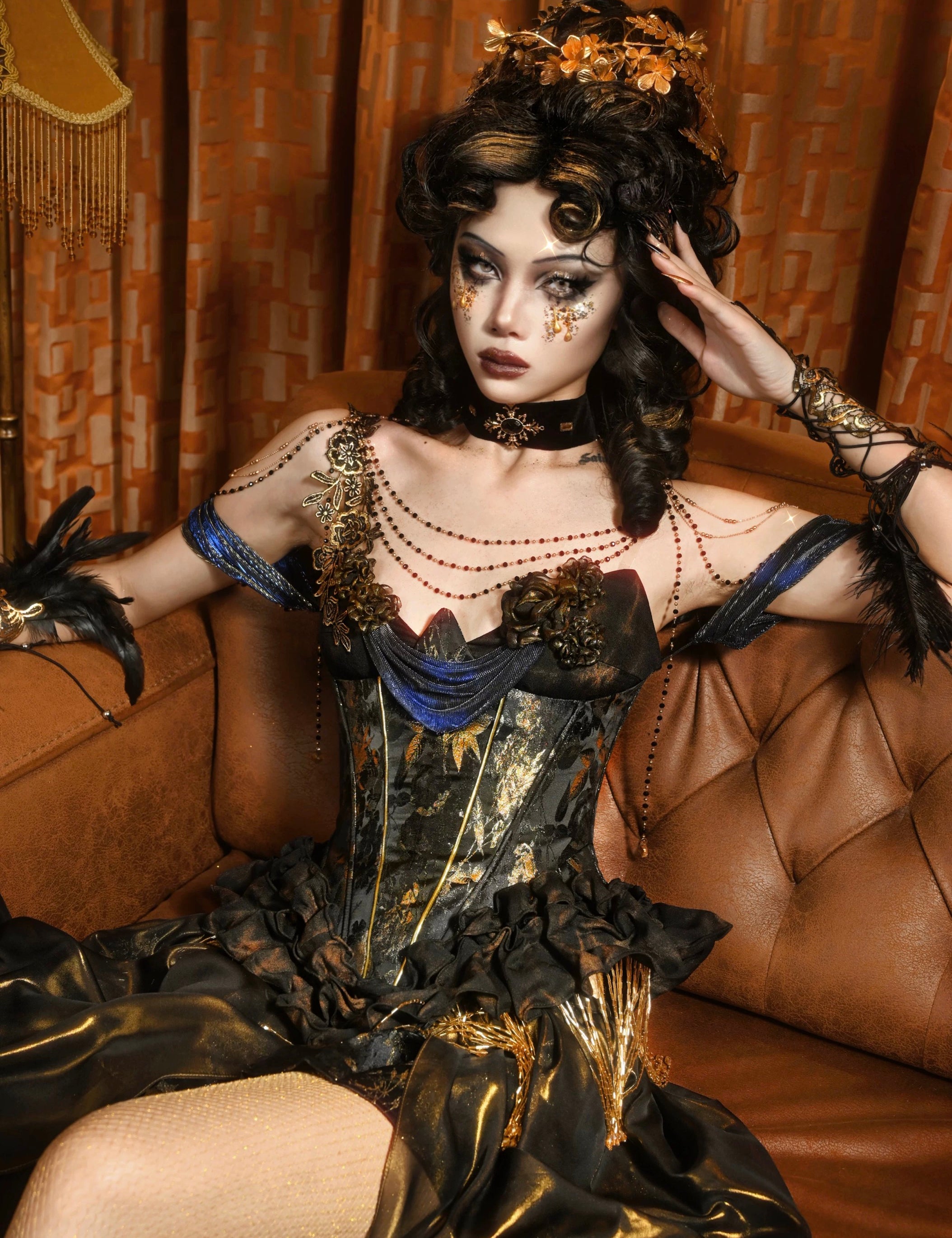 Woman in a dark, ornate Blood Supply Golden Hour Baroque Corset with gold accents sitting on a brown couch.
