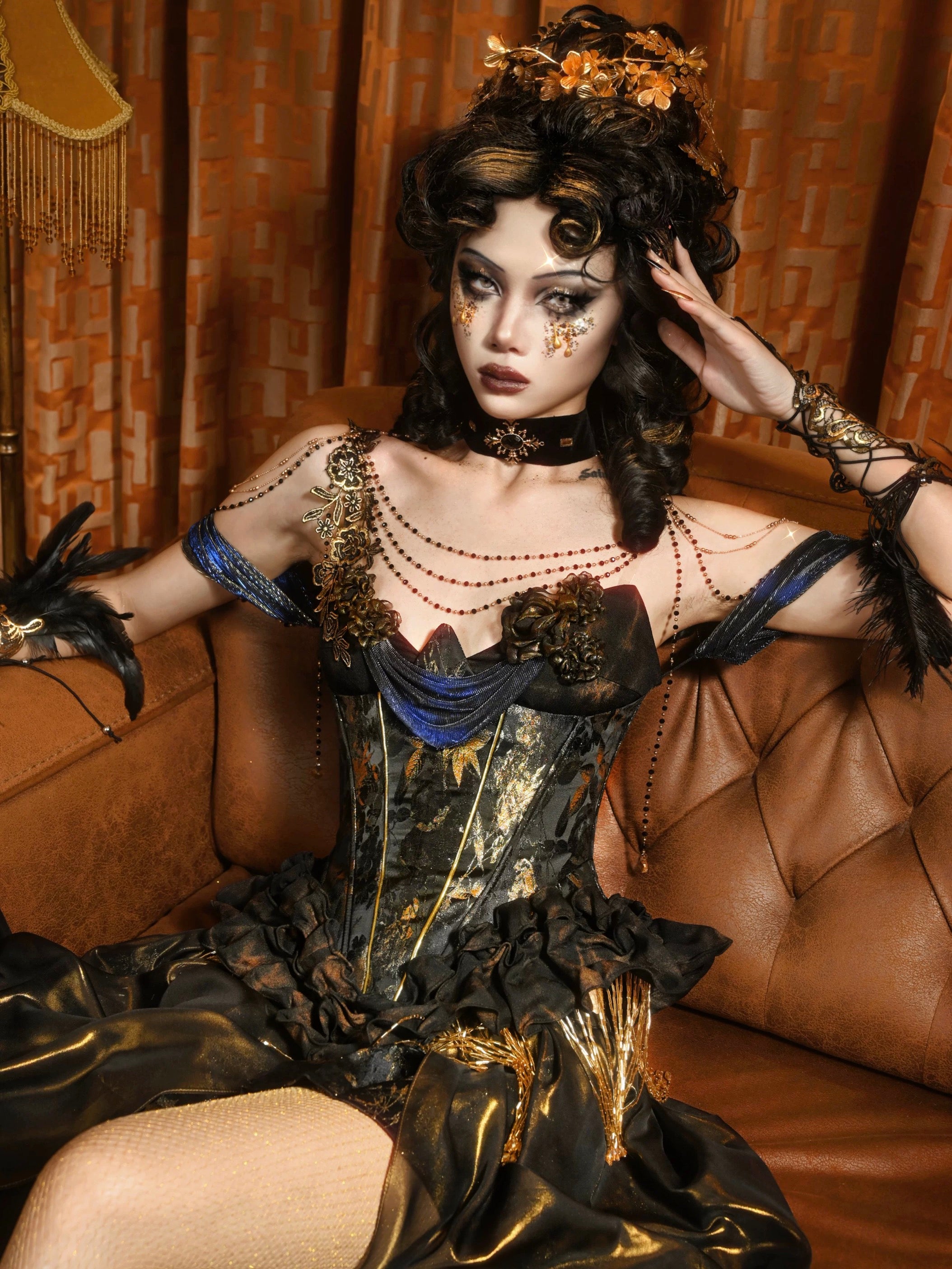 Woman in a dark, ornate Blood Supply Golden Hour Baroque Corset with gold accents sitting on a brown couch.