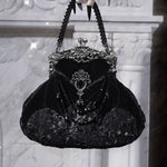 Black velvet handbag with intricate detailing held by a gloved hand against a textured white background