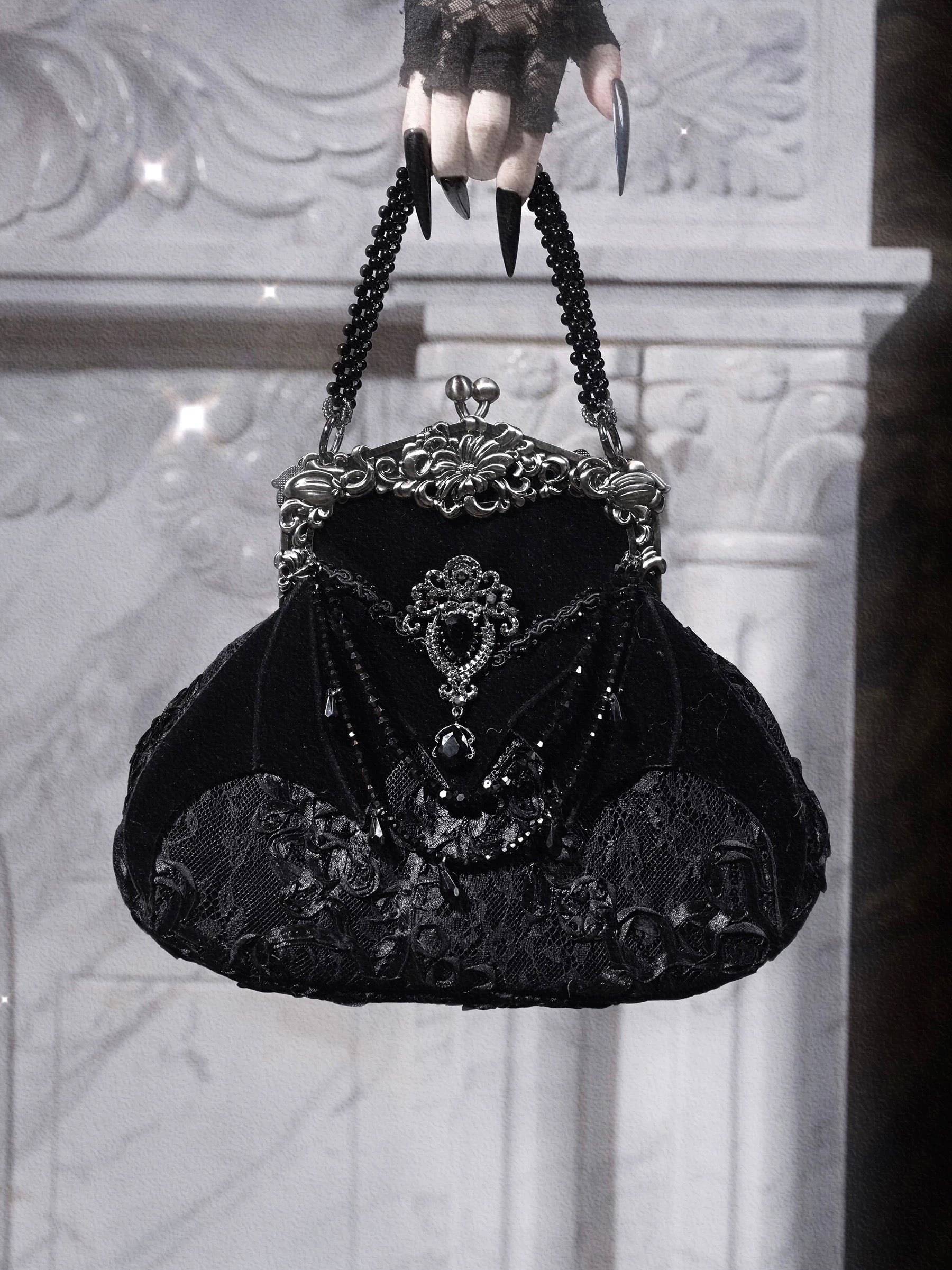 Black velvet handbag with intricate detailing held by a gloved hand against a textured white background