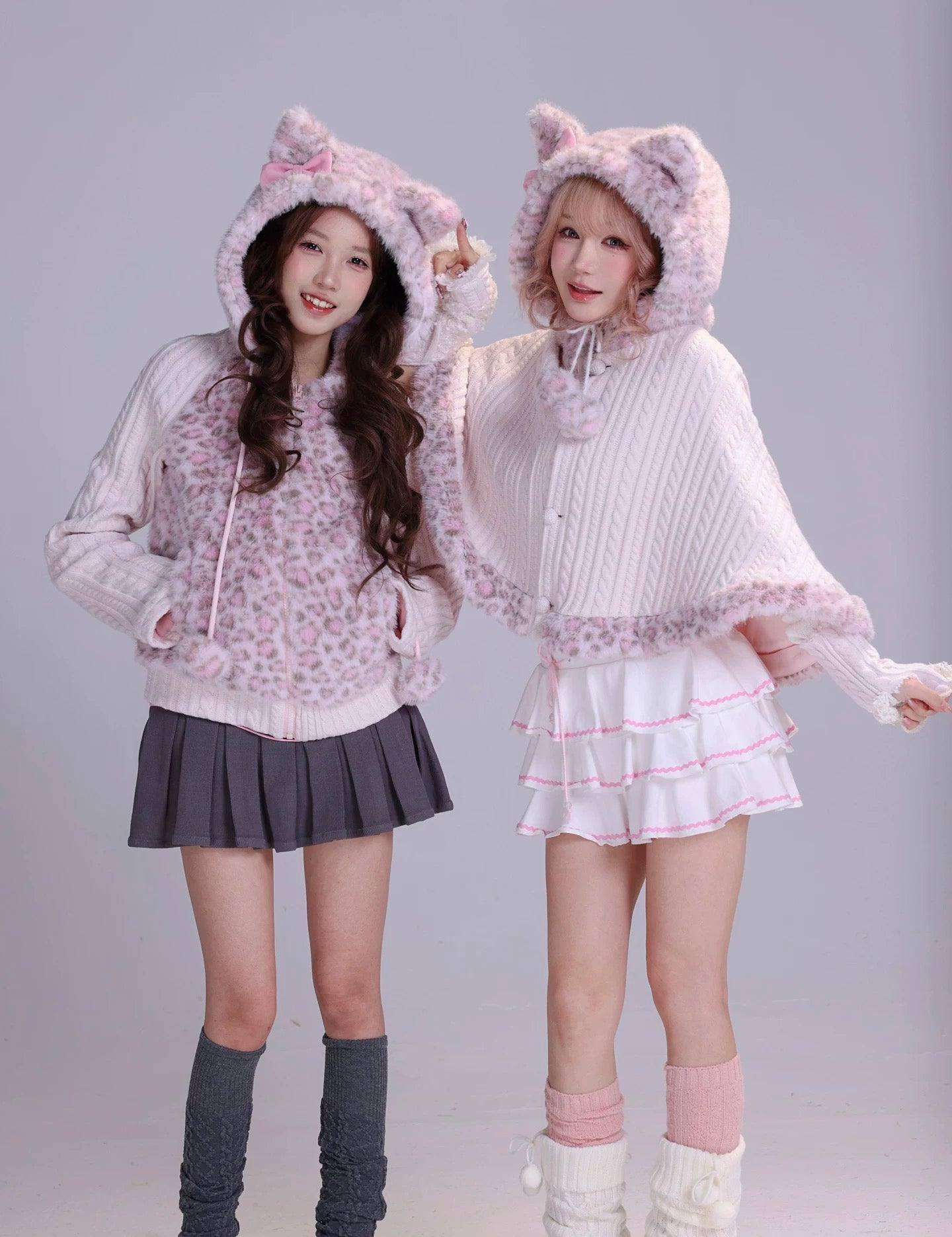 Two women wearing matching cat-themed outfits with  cat ears on hoodies in fluffy faux fur fabric and mini skirts 