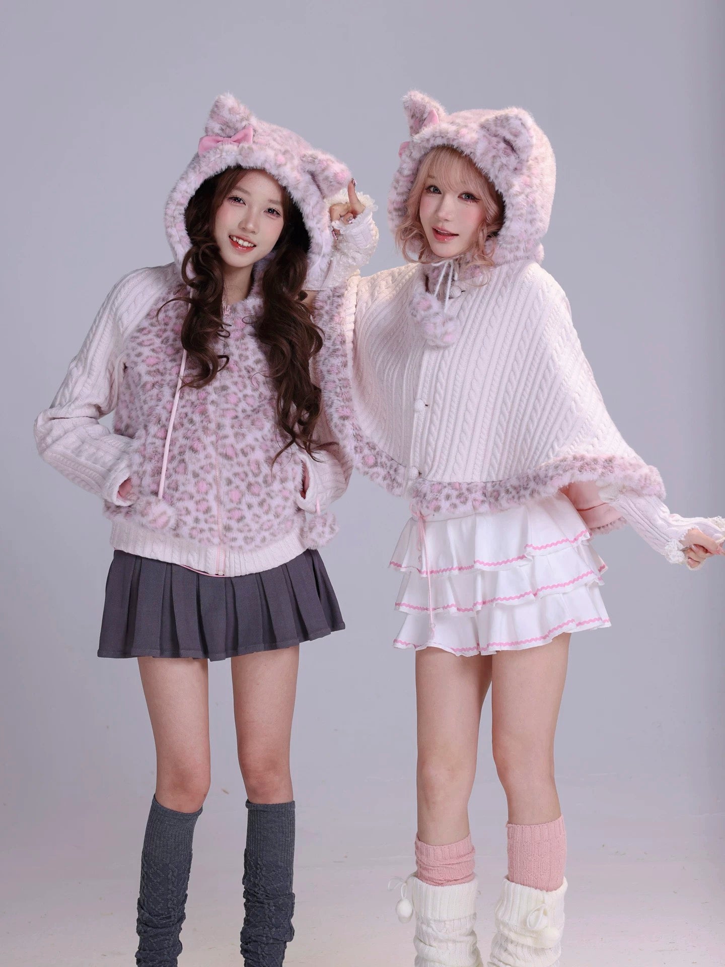Two women wearing matching cat-themed outfits with  cat ears on hoodies in fluffy faux fur fabric and mini skirts 