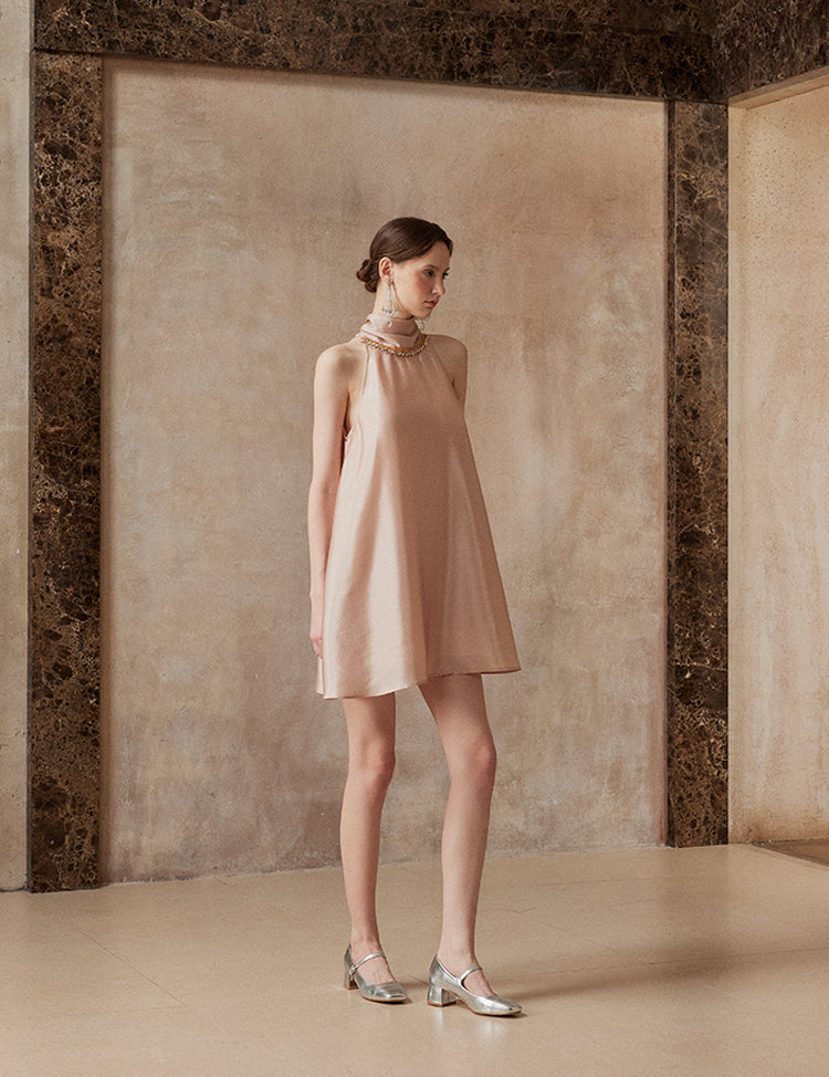 Woman wearing a beige dress standing against a textured wall.