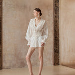 Woman in a white outfit standing against a textured wall.
