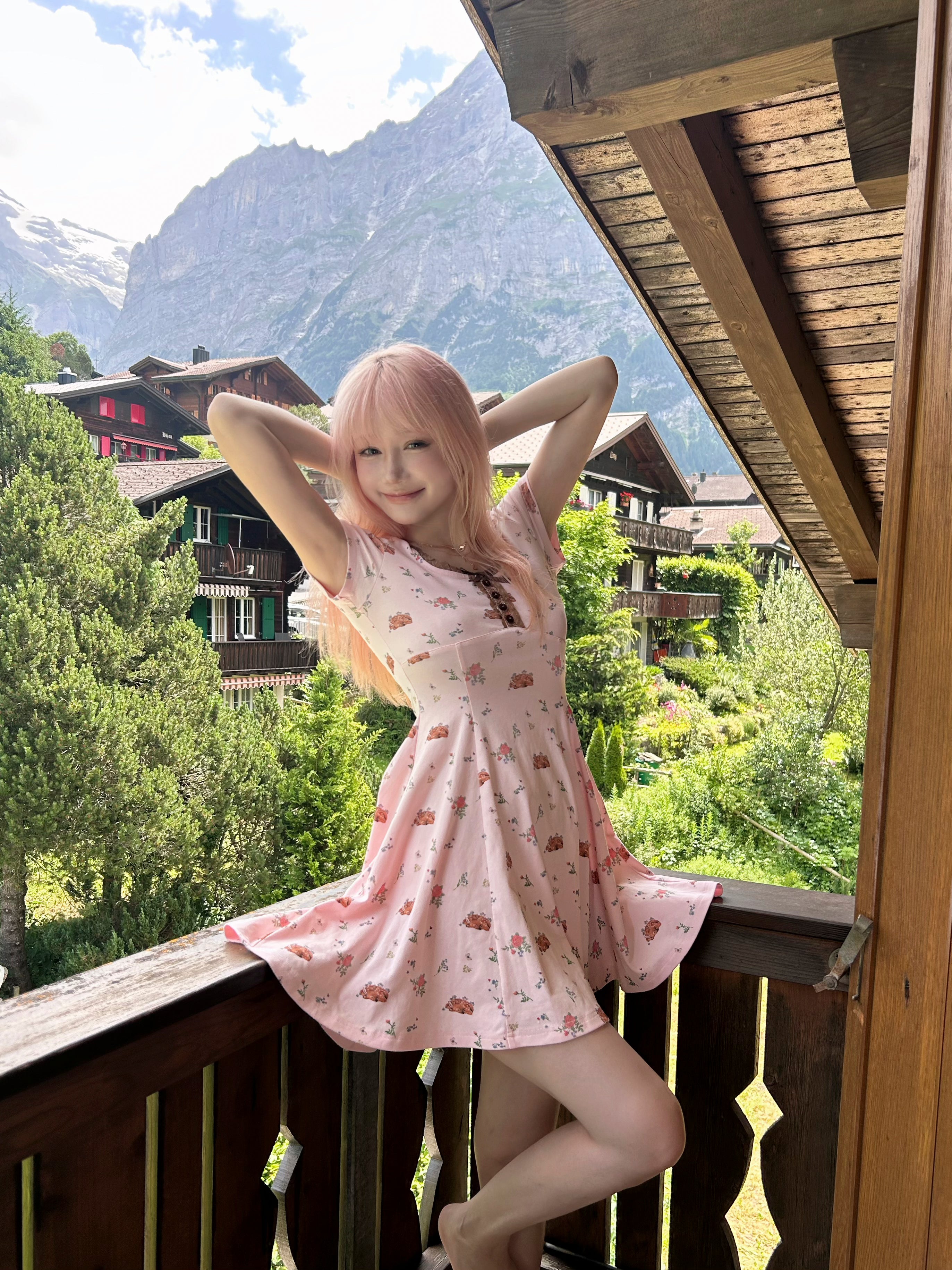 Woman in a pink deer print dress standing on a balcony with mountains in the background