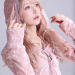 Woman wearing a pink hooded outfit with a sheer overlay against a light gray background