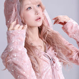 Woman wearing a pink hooded outfit with a sheer overlay against a light gray background