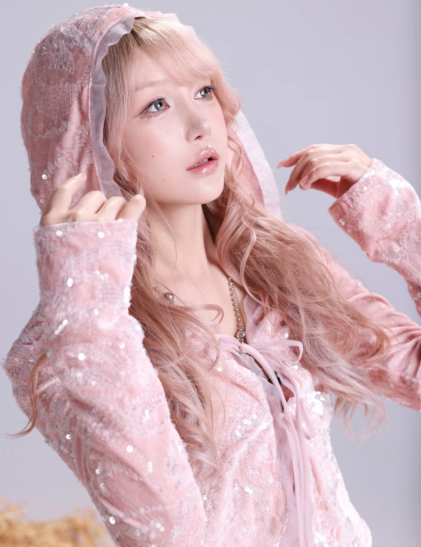 Woman wearing a pink hooded outfit with a sheer overlay against a light gray background