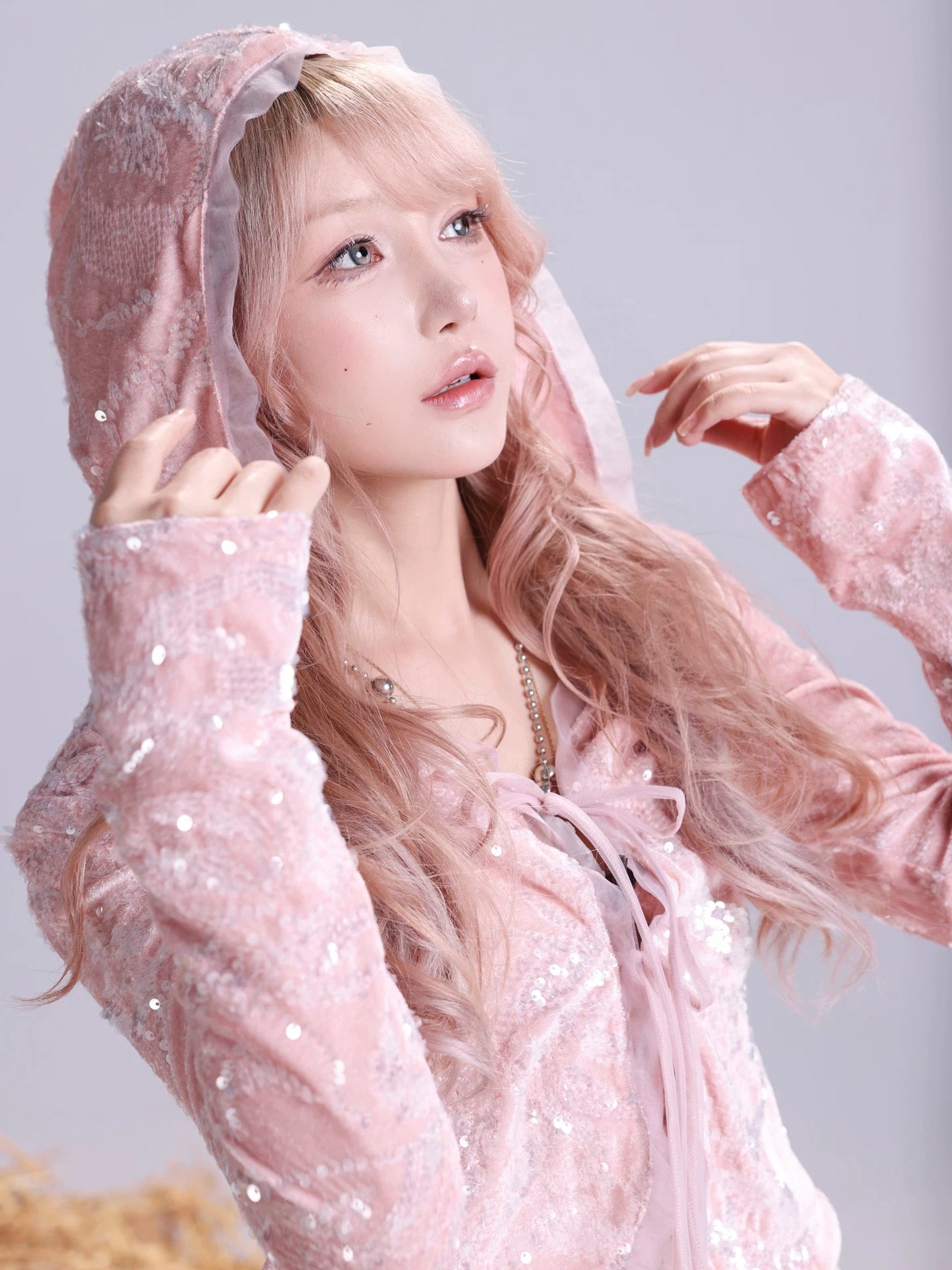 Woman wearing a pink hooded outfit with a sheer overlay against a light gray background