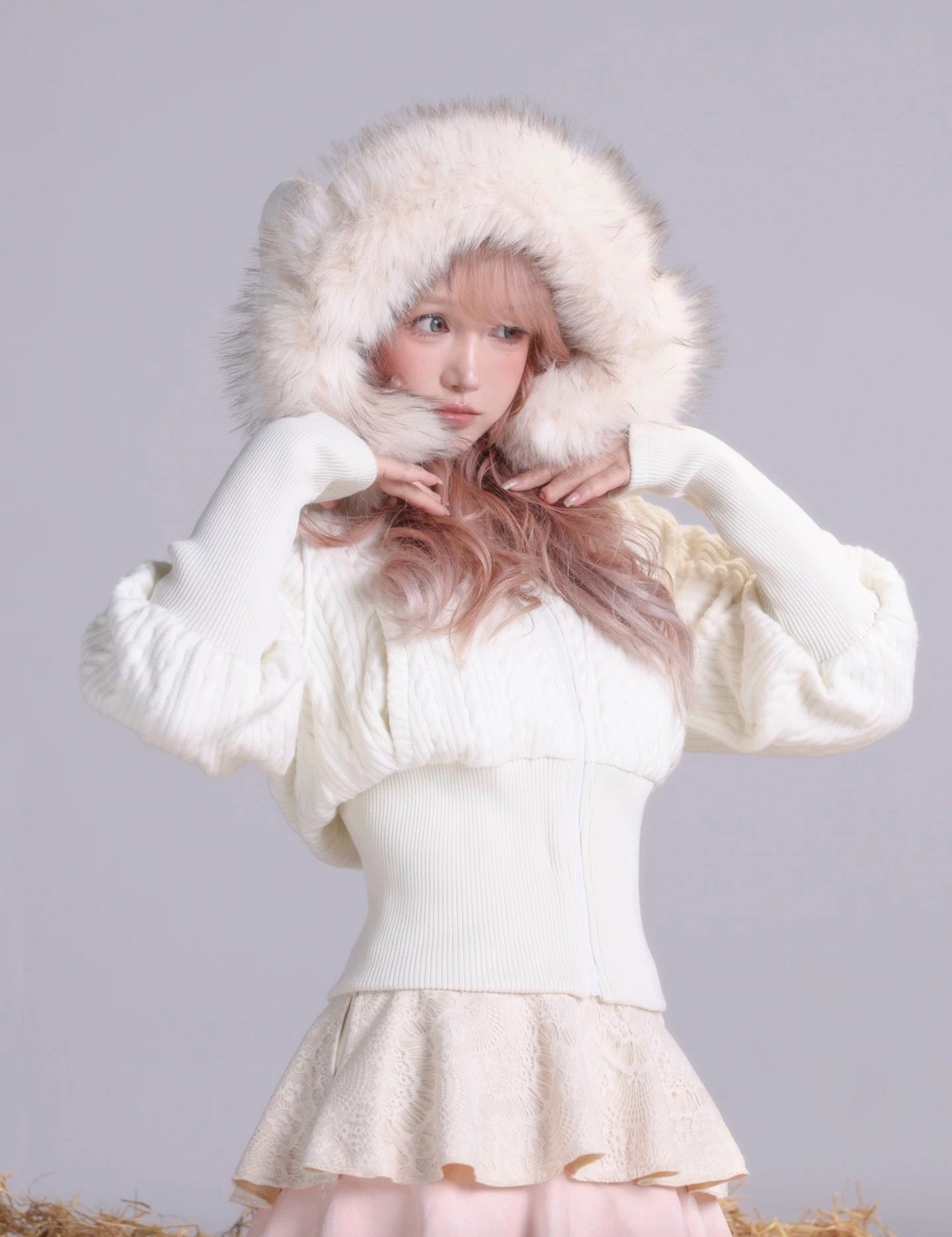 Girl wearing a white  faux fur coat with sheep ears on hood on a gray background