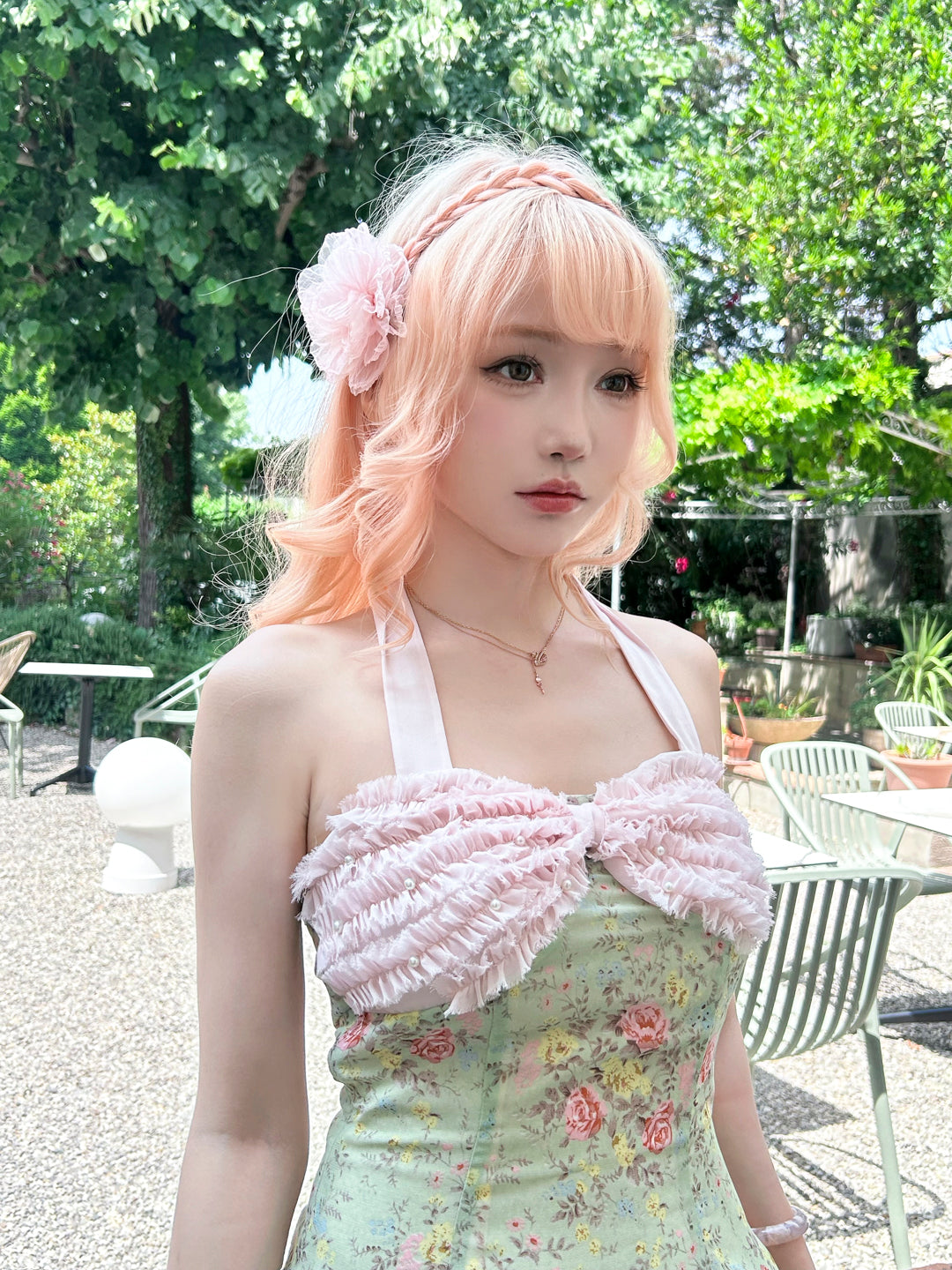 Woman with pastel pink hair and floral headband wearing a floral dress outdoors.