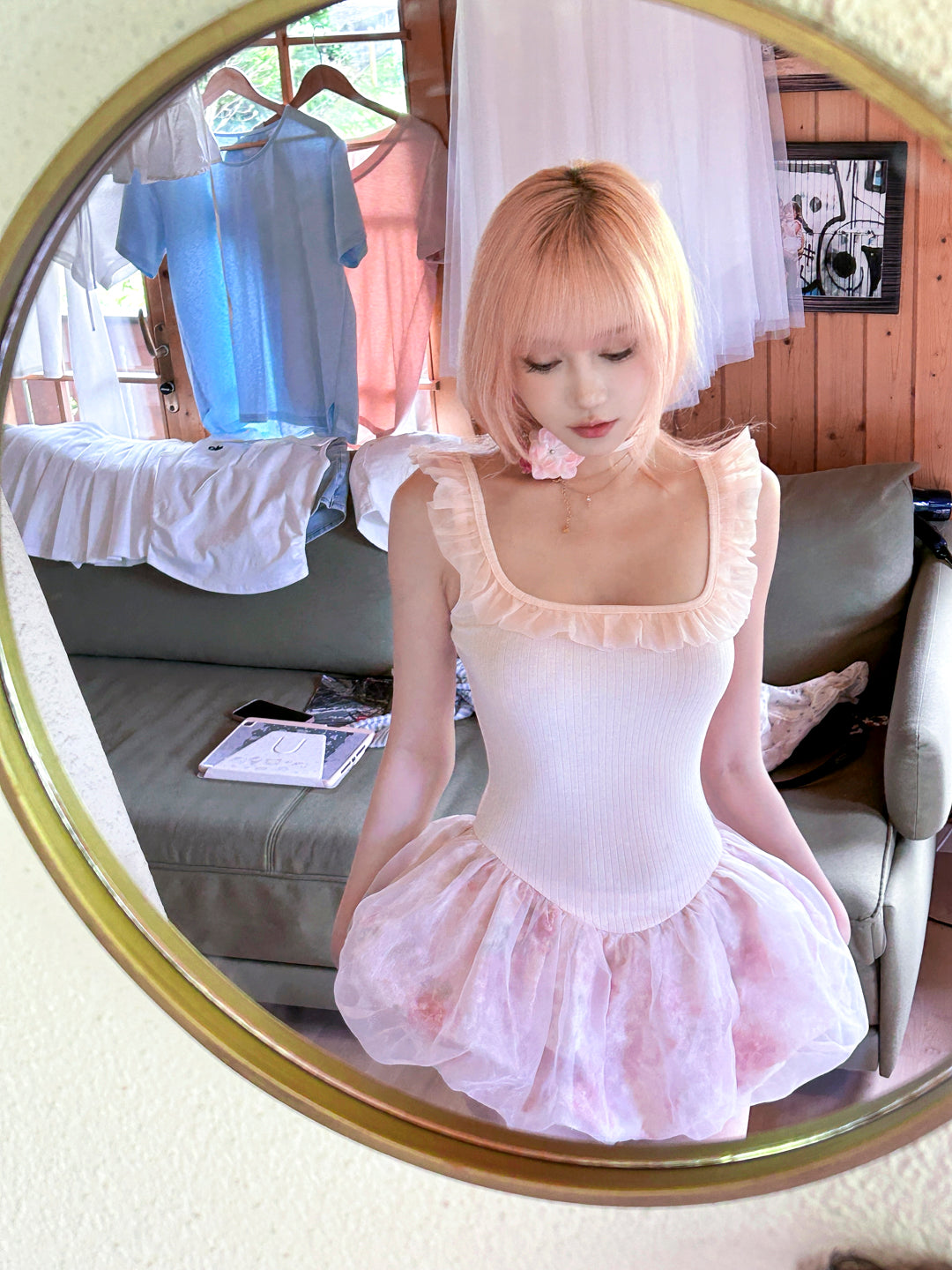 Woman in pink hair wearing a pastel pink ballet  dress with floral pattern outfit in front of a mirror.