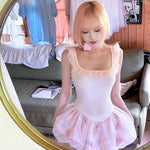 Woman in pink hair wearing a pastel pink ballet  dress with floral pattern outfit in front of a mirror.