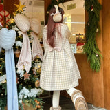 Girl wearing a checkered coat and white gloves in front of a decorated Christmas tree.
